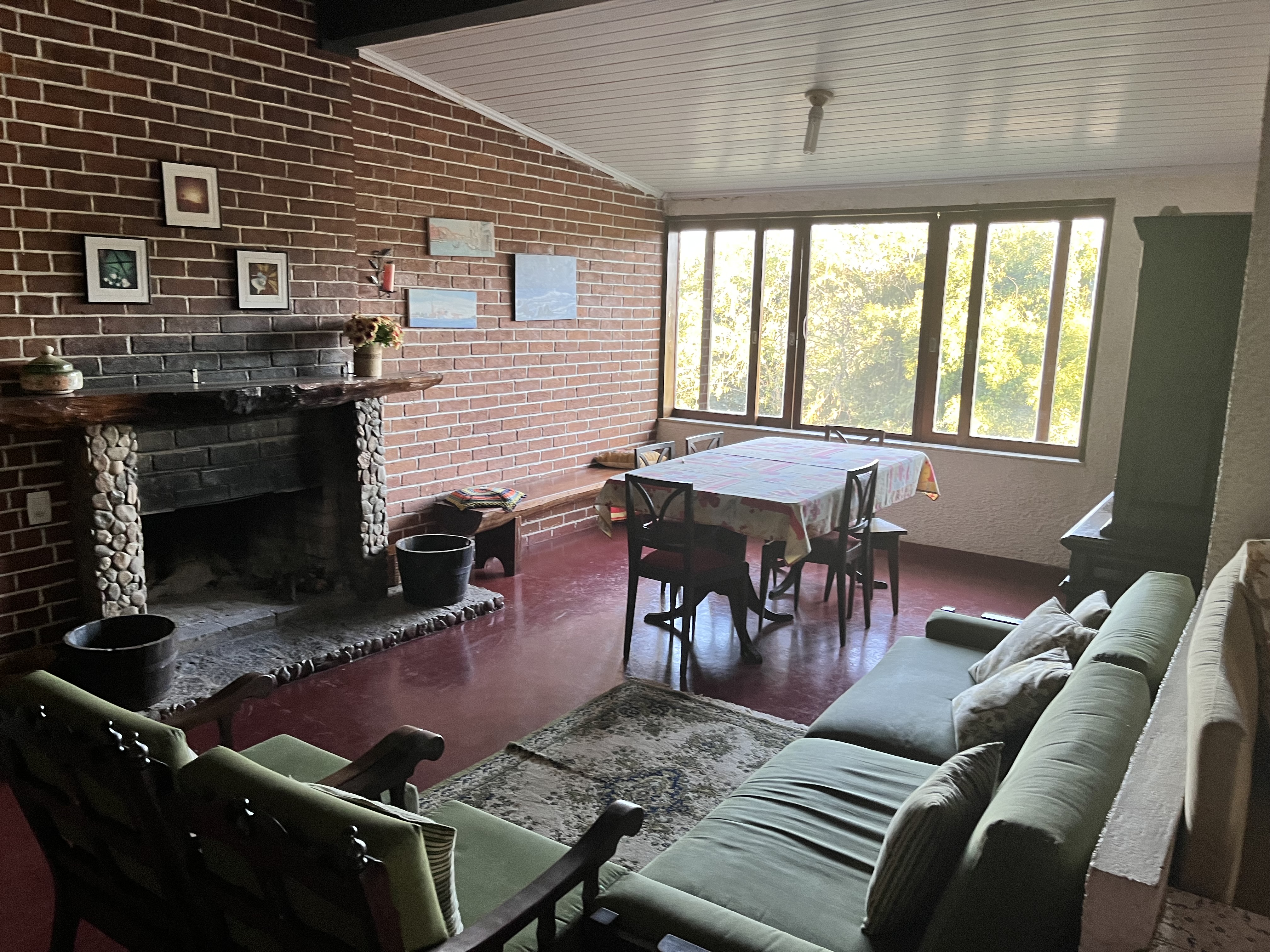 Sala da Casa Capelinha com lareira, janelas para o verde e clima de casa de serra