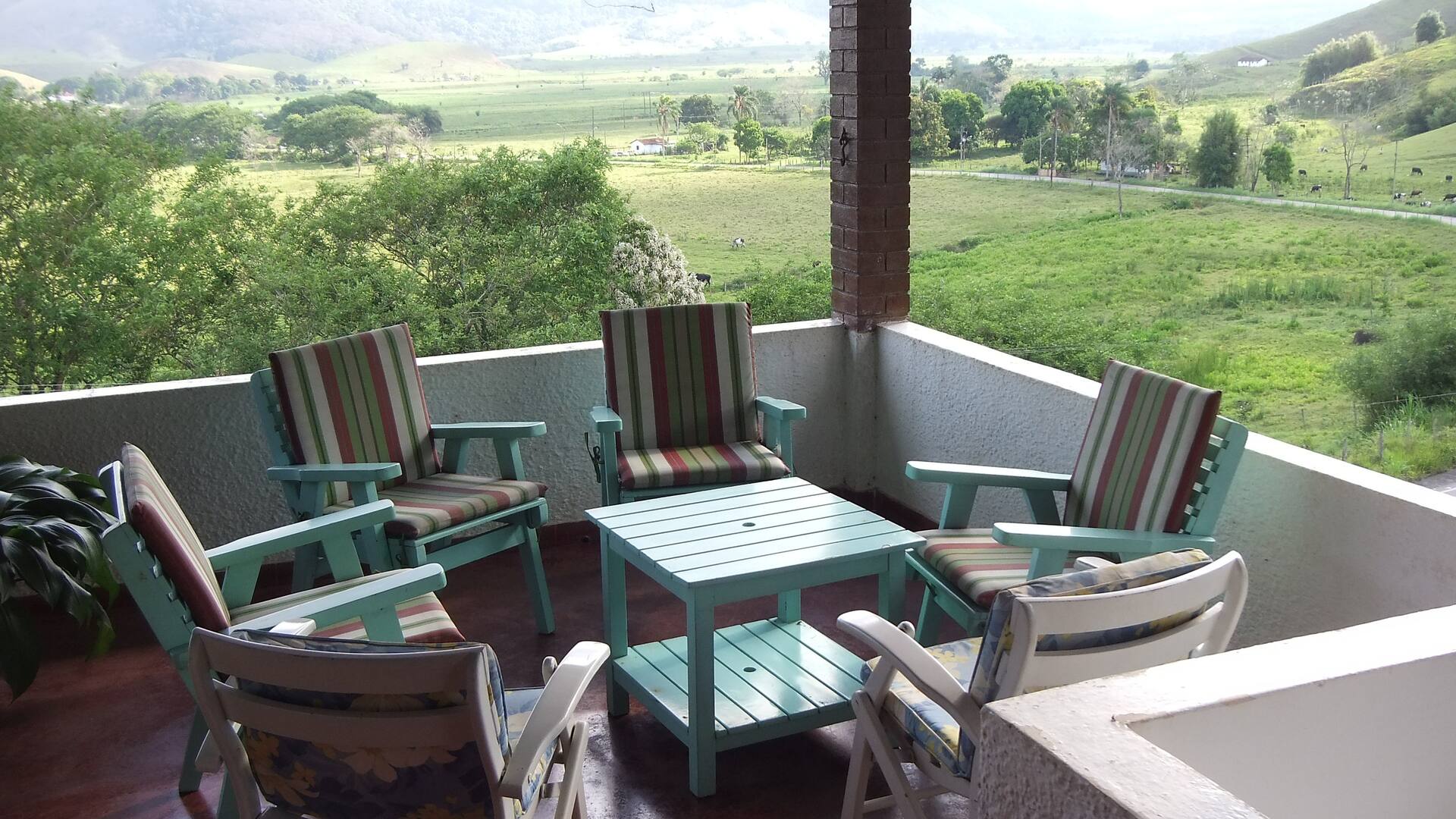 Varanda da Casa Capelinha com poltronas, vista para a serra e área verde em Resende